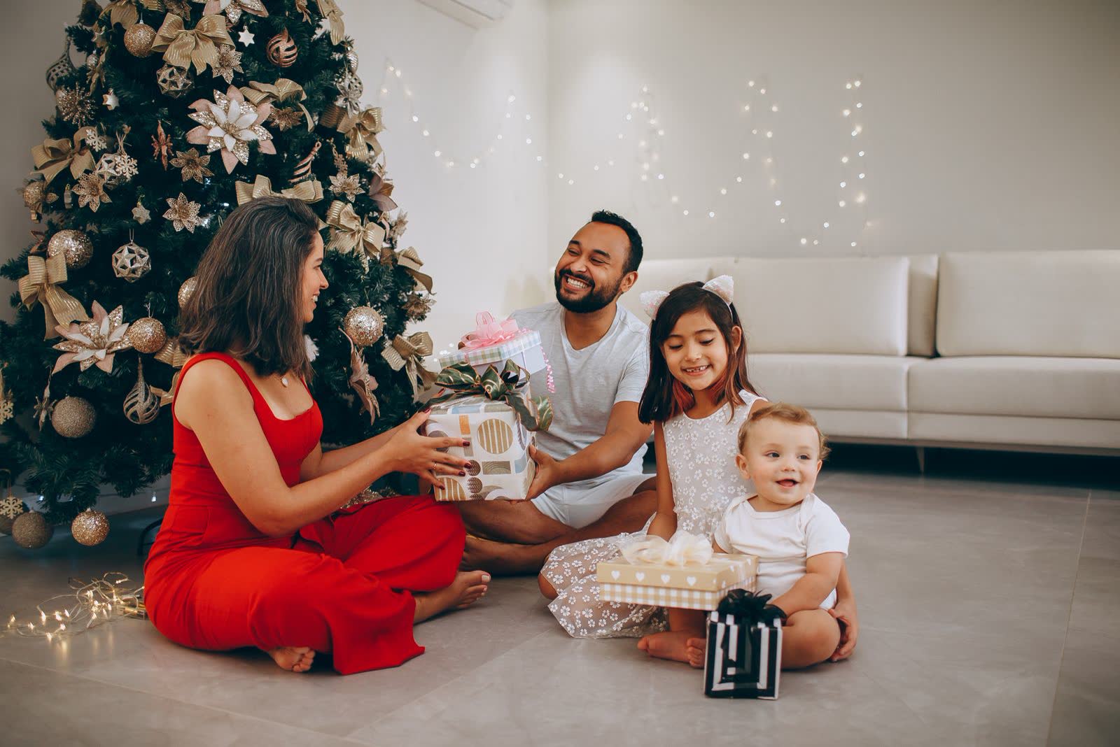 Parents, a girl and a baby swapping gifts by the Christmas tree at home