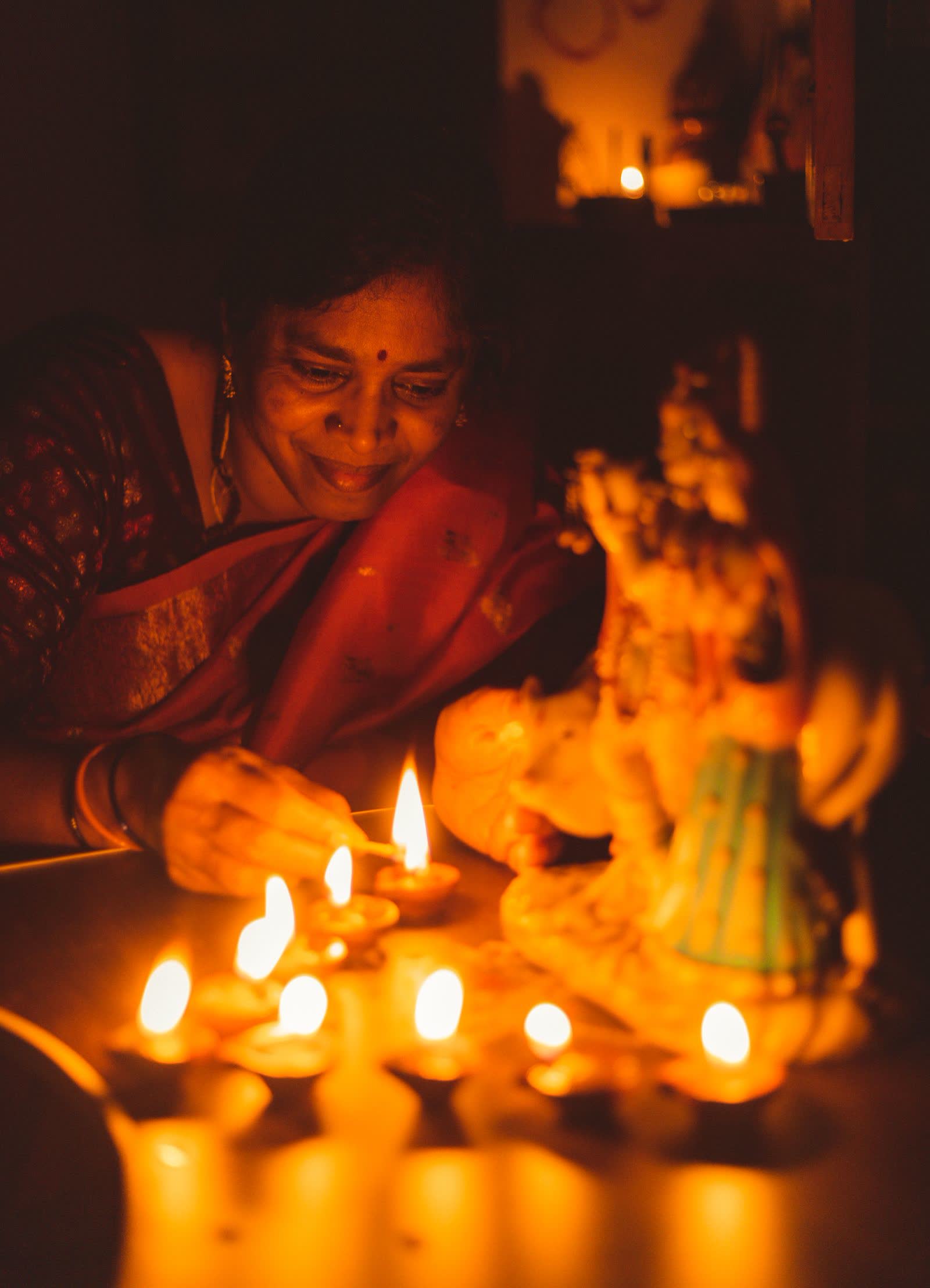 An older woman smiling as she lights rows of diyas