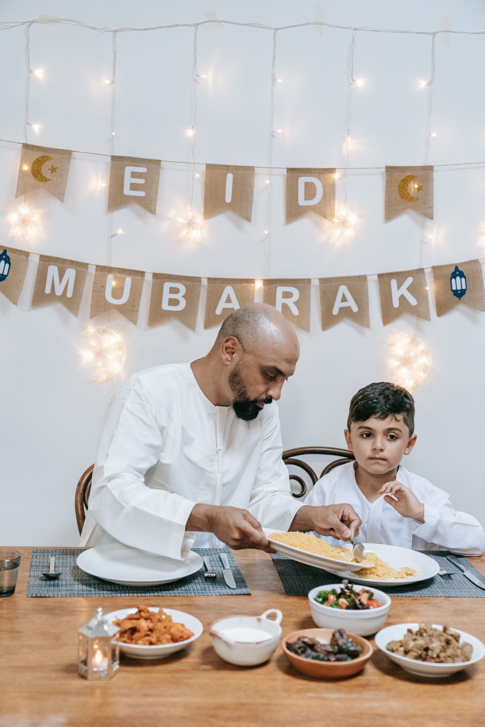A father serving his son at an Eid meal under an Eid Mubarak banner