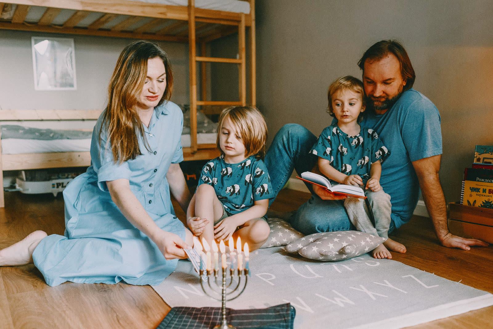 Parents and two small children on the floor at home beside a lit menorah