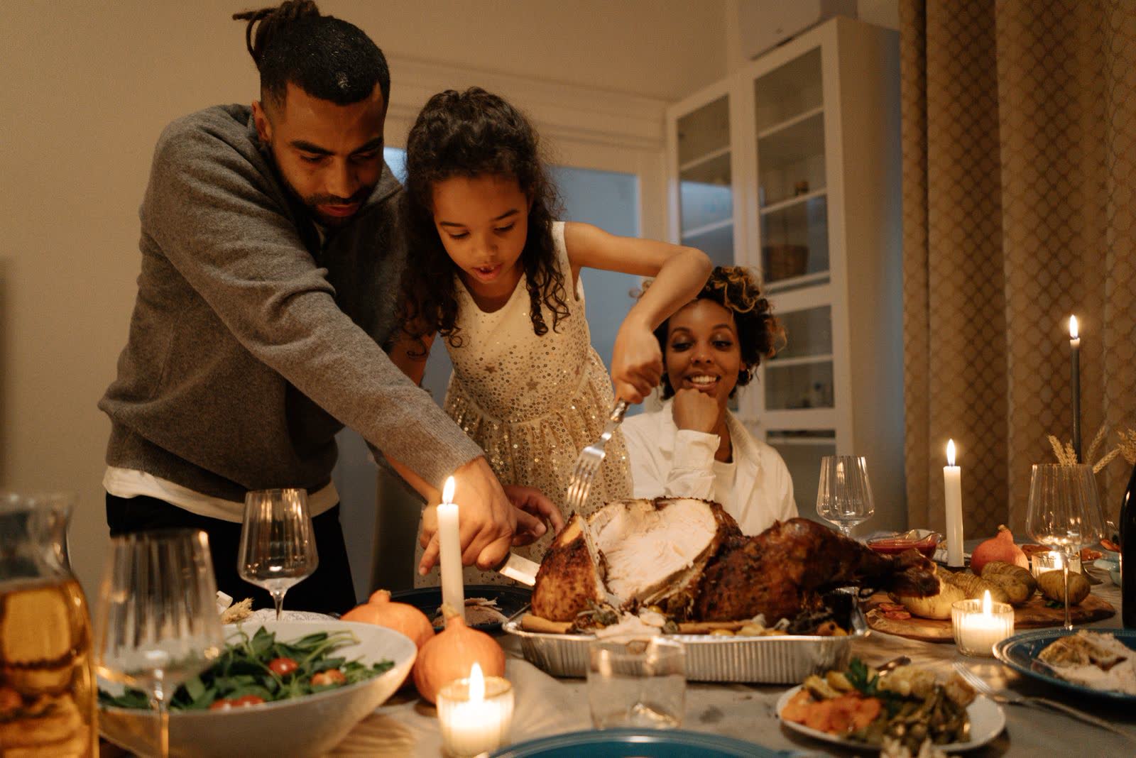 A father and daughter carving a turkey by candlelight while the mother laughs