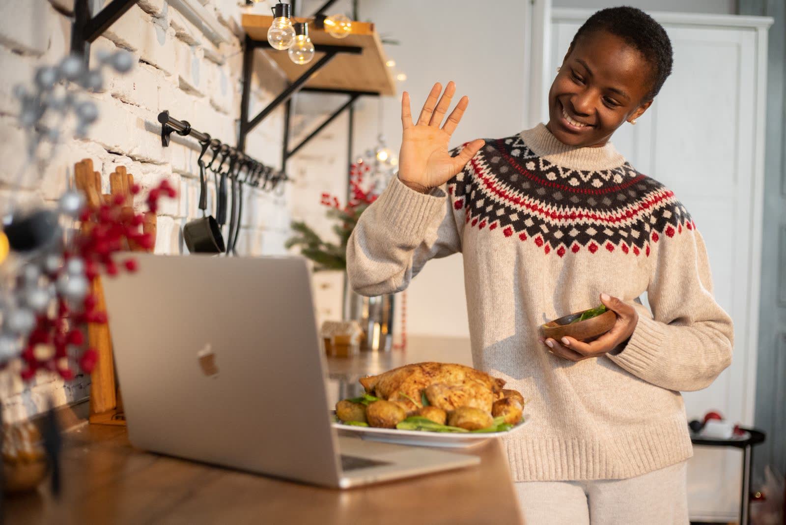 A woman in a holiday sweater waving at a laptop beside a roast